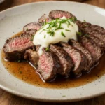Medium-rare beef Delmonico steak with melted herb butter on a neutral plate